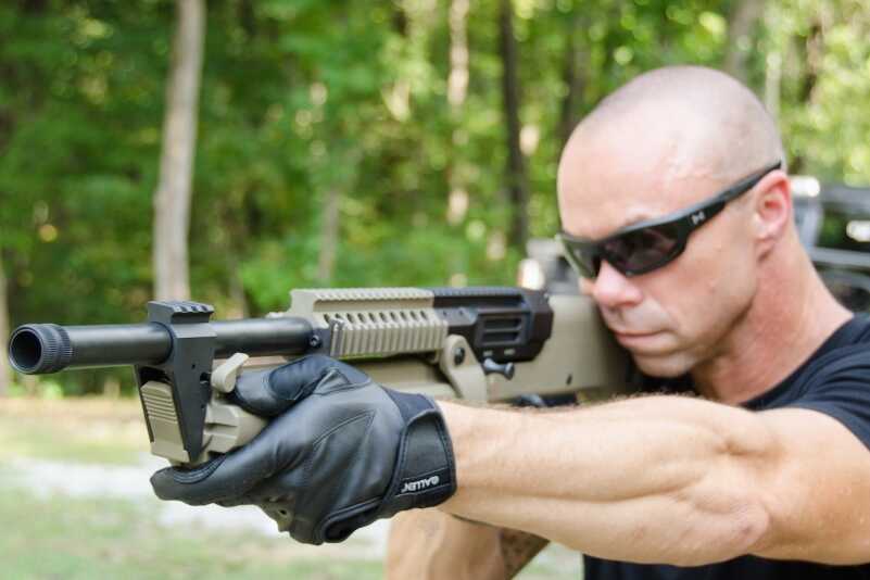 The shooter's support hand is located far forward ready to engage the dual levers (forward of this thumb) that allow the revolving magazine to be rotated. 