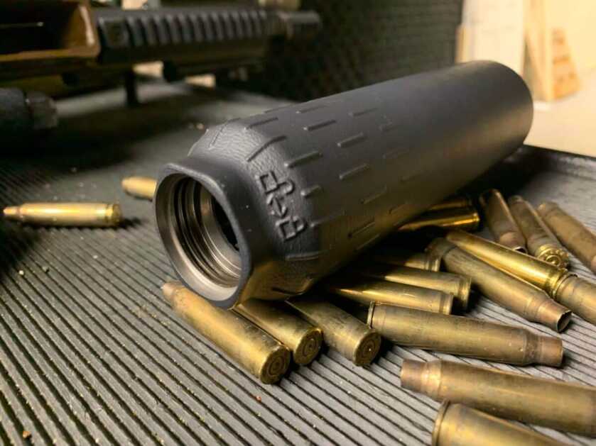 A HuxWrx Flow 762 Ti suppressor rests on a table surrounded in rifle brass.