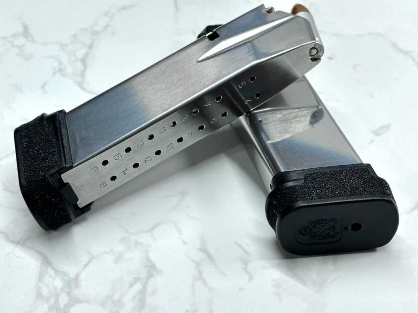 Two magazines lay crossed. The bottom one is unloaded and the top one is filled to capacity with 9mm.