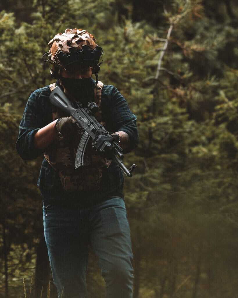 AK Buyers Guide Man in tactical gear holding an AK outside under tree foliage