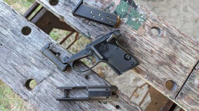 Beretta Tomcat with parts around it set on aged wood