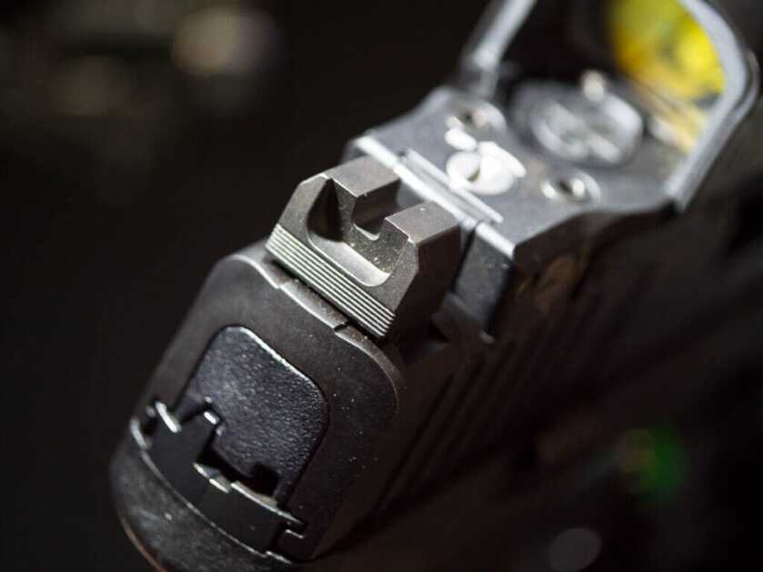 Close up of the rear sights which are blacked out and serrated. There is a red dot on top of the slide.