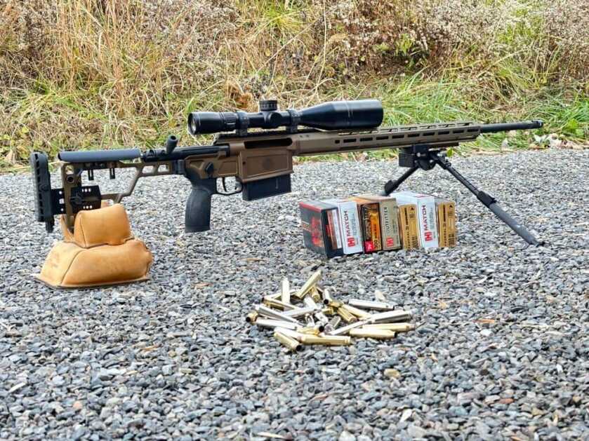 A rifle sits on a bipod and rear bag, behind an assortment of ammunition.