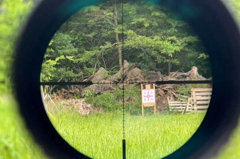 Looking through a scope reticle at a target and some trees