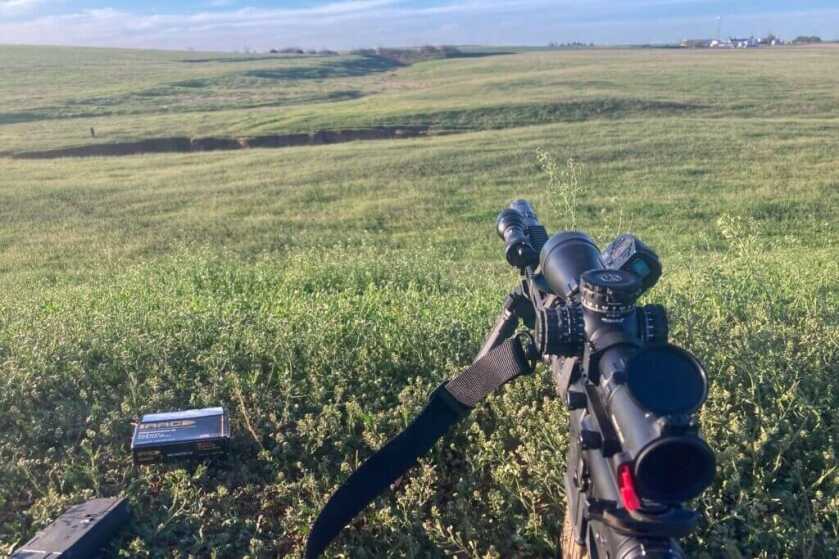 Primary Arms GLX 2.5-10 mounted to a rifle read to shoot long range in an open field