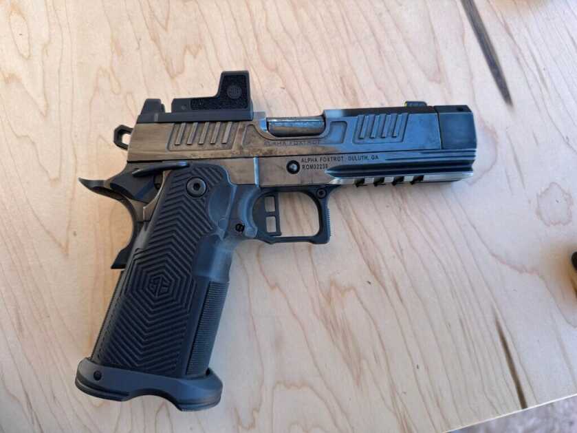 A highly polished black handgun sits on a wooden table, pointing to the right. 