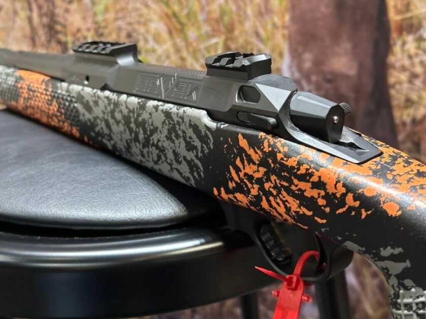 Closeup shot of a rifle action. The stock is a orange and grey camo.