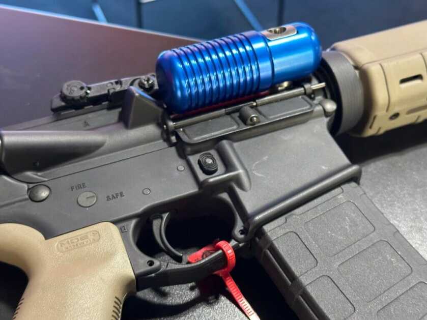 A blue tank sticks out of the ejection port of a black AR15.