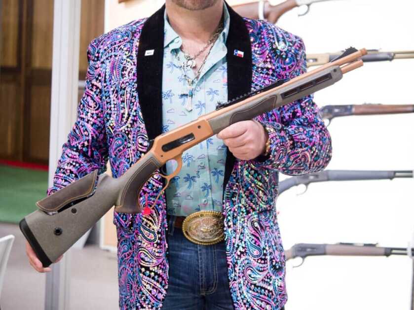 The whole gun facing to the right, held by a cowboy wearing a purple sequin jacket.