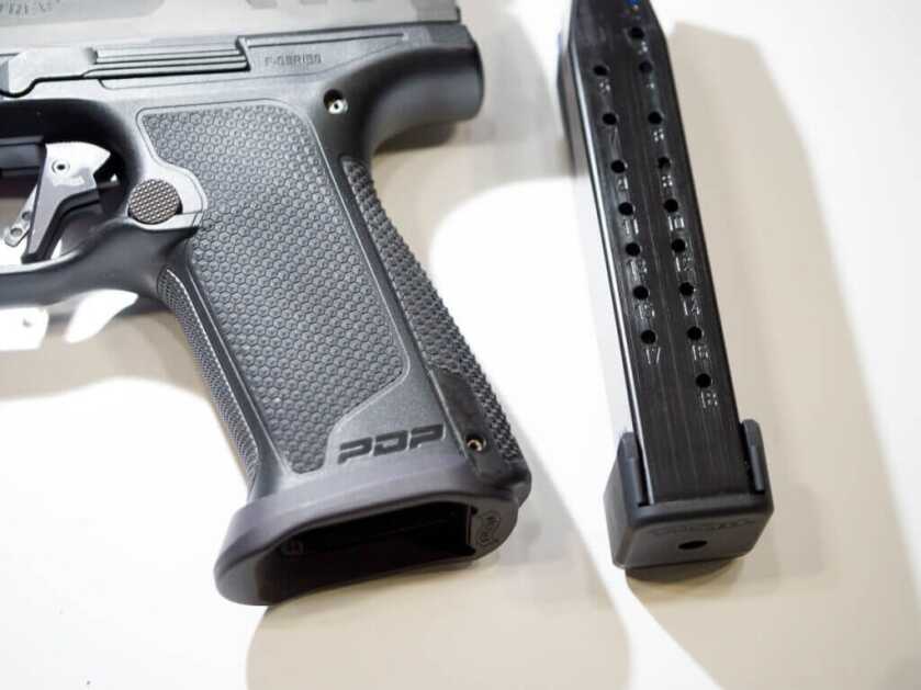 Close up of the grip with a magazine laying next to the gun.