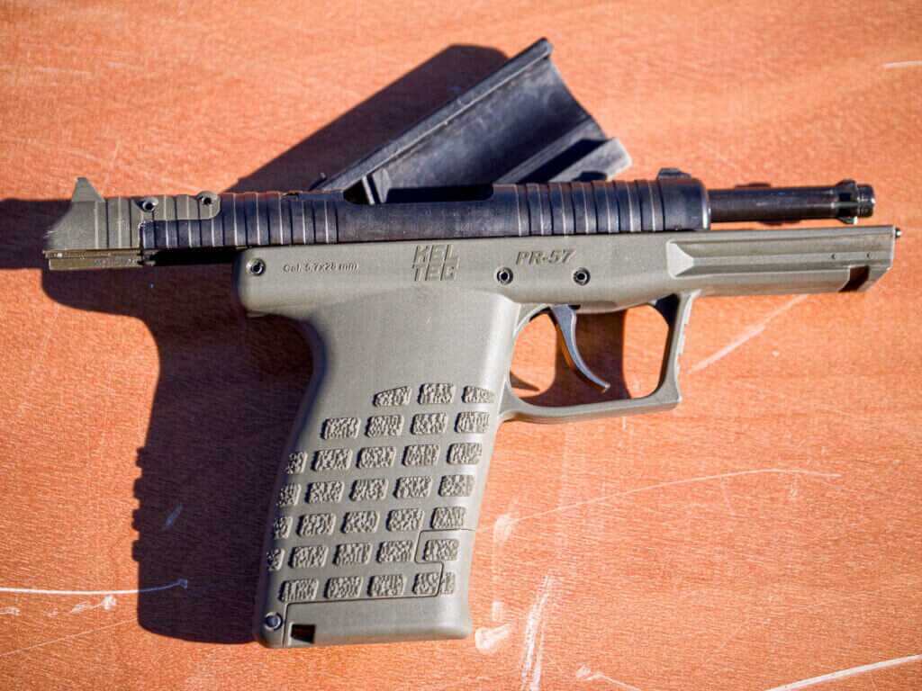 The gun is laying on a table with the right side facing up. The slide is locked open showing the rotary barrel. the stripper clip is propping the gun up.