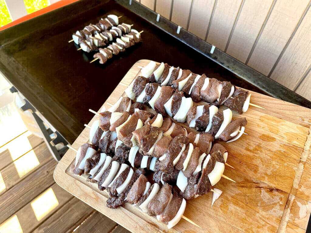 meat and onions skewered on sticks waiting on a cutting board to go onto the griddle.