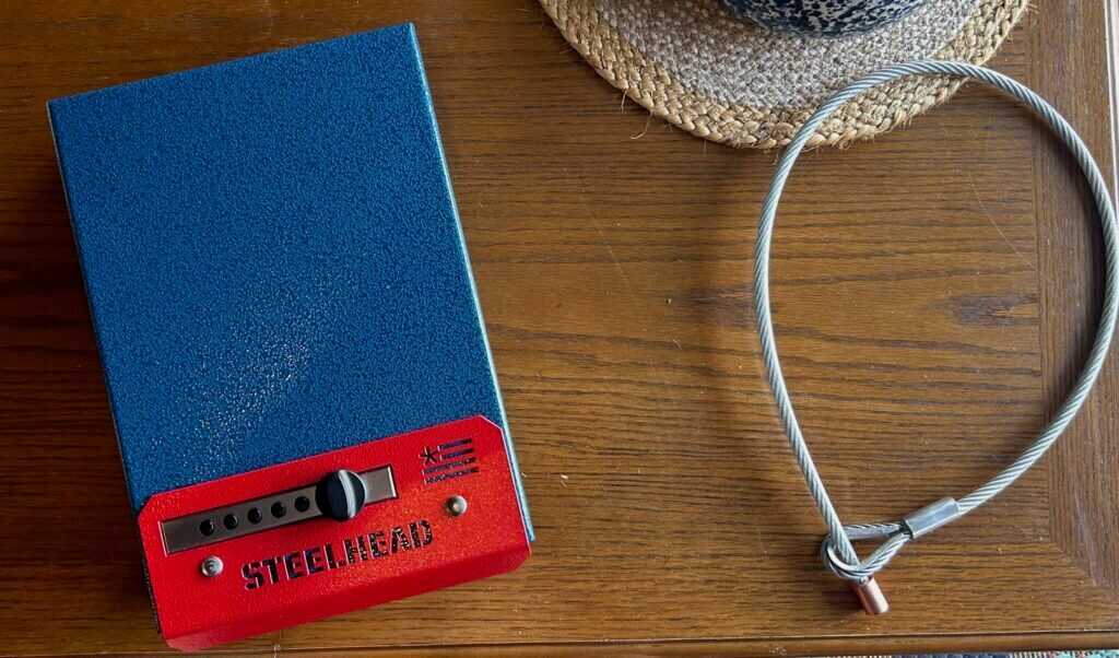 Steelhead Outdoors Founder’s Edition pistol lock box and heavy-duty cable on wood table.