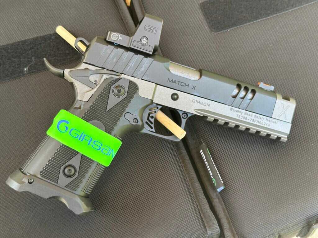 A black and silver handgun with an optic is posed against a black background.