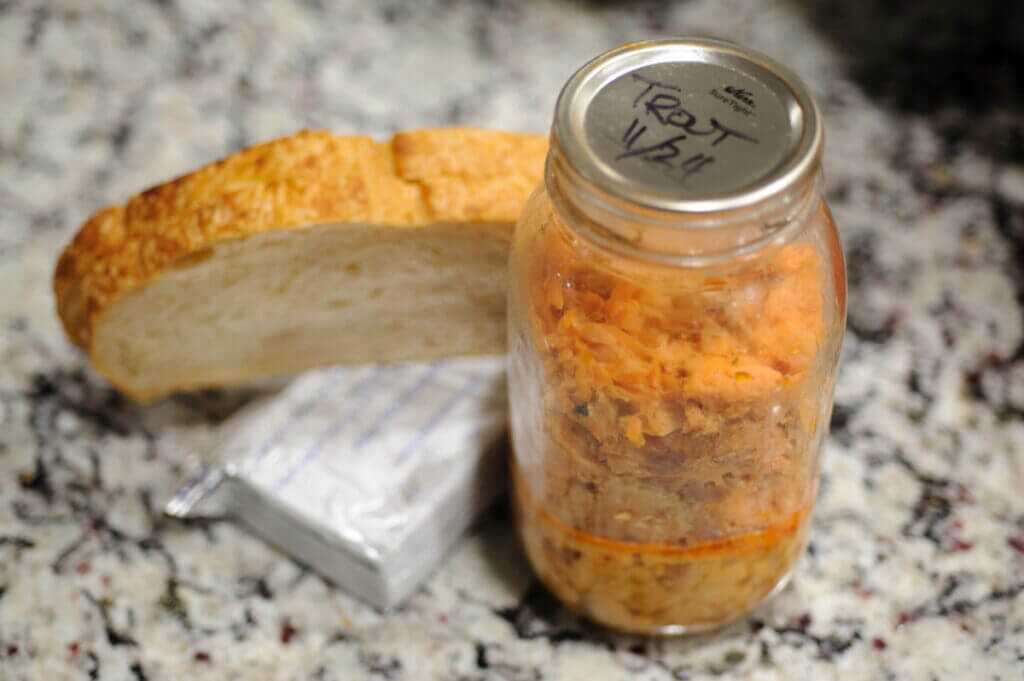 Canned smoked trout, cream cheese, sliced sourdough, and cheese laid out before making a grilled fish sandwich.