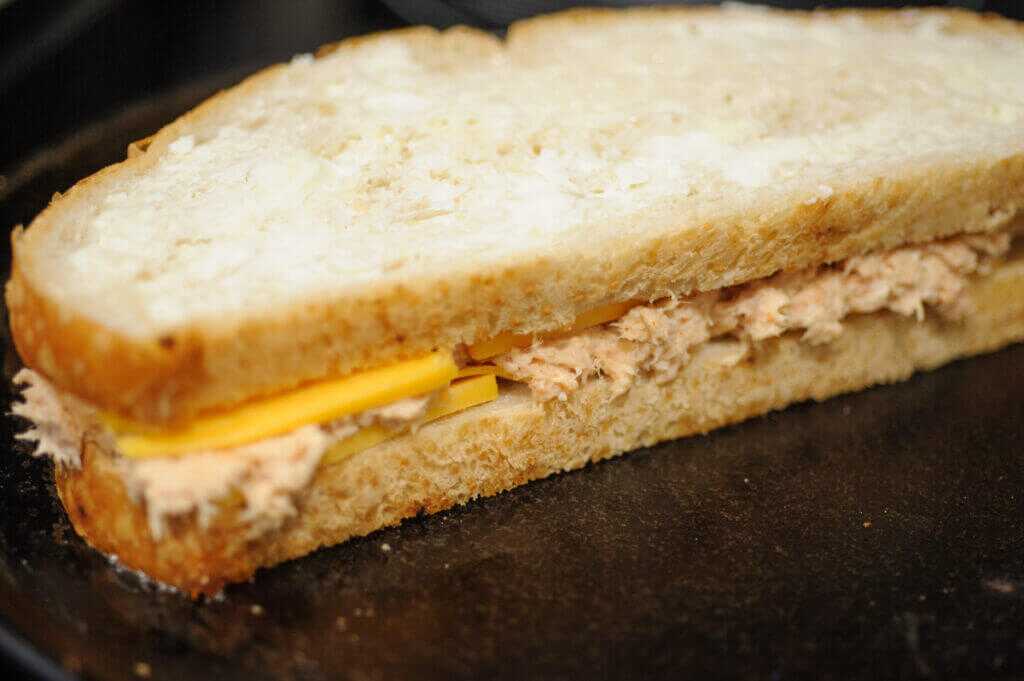 Assembled trout melt on a hot griddle with cheese, ready to press and toast.