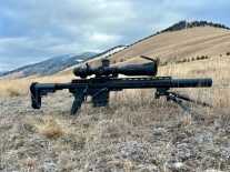 A black bolt-action rifle is staged on a mountaintop for pictures.