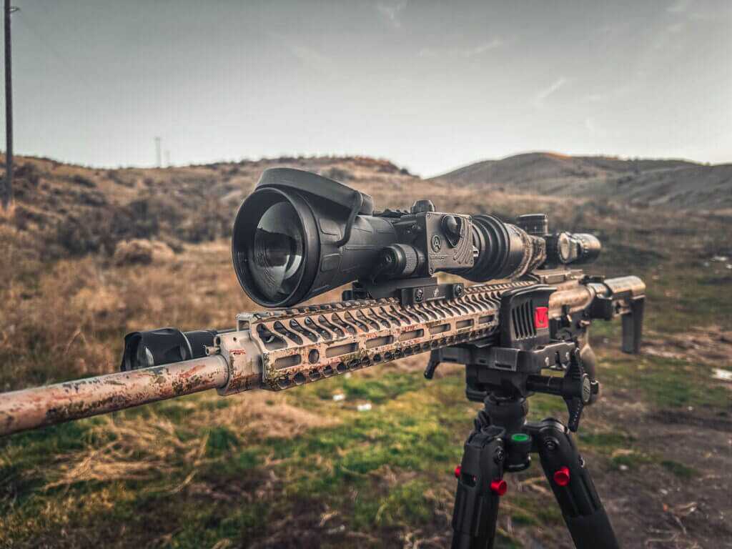 Thermal riflescope mounted on a bolt-action rifle on a tripod, illustrating night vision vs thermal choices