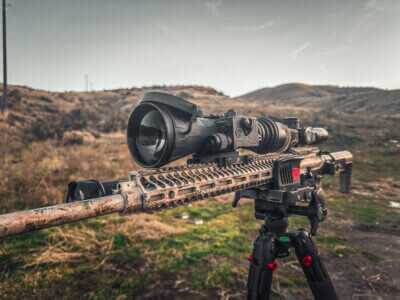Thermal riflescope mounted on a bolt-action rifle on a tripod, illustrating night vision vs thermal choices