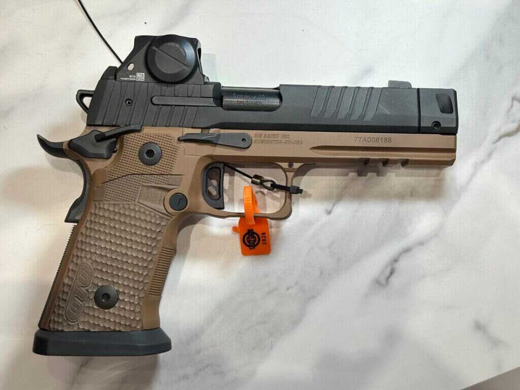 A tan and black handgun rests on a white marble countertop.