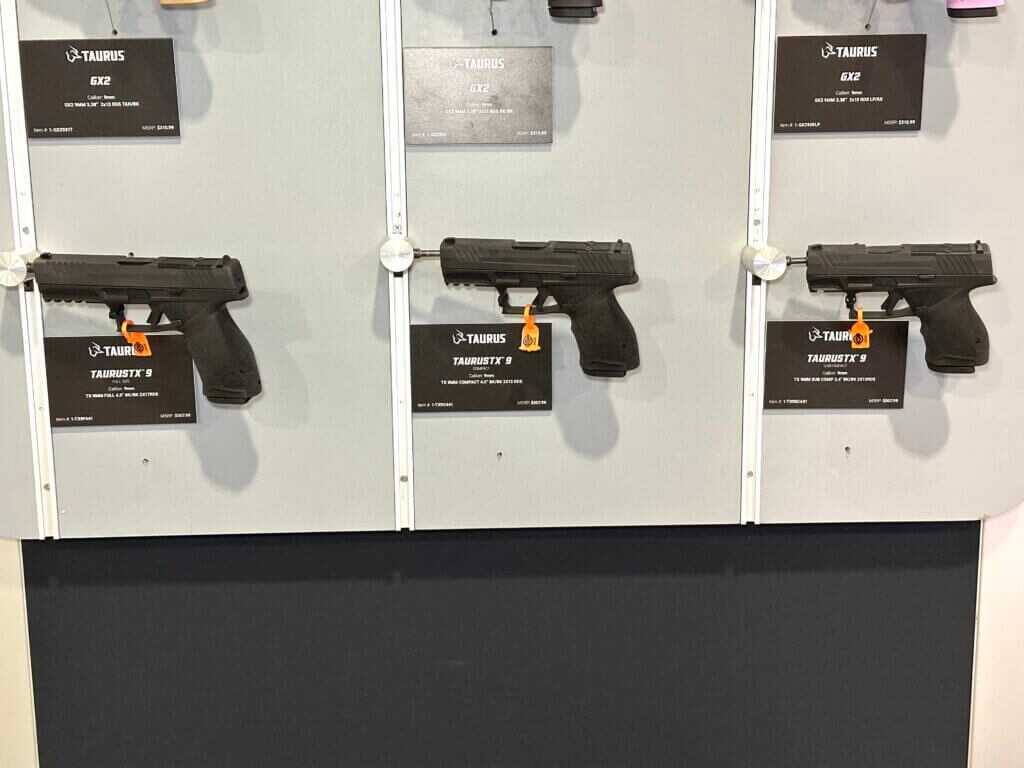 Three different pistols are hanging off of a wall display. They are arranged in order of biggest to smallest.