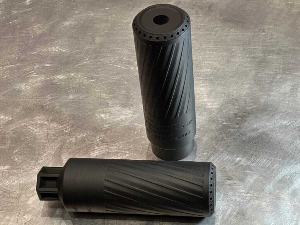 Two suppressors sit on a steel tabletop.