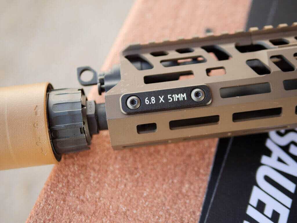 Close up view of the left side of the end of the barrel and handguard of the M7 with a supressor attached. There's a plate reading 6.8x51mm.