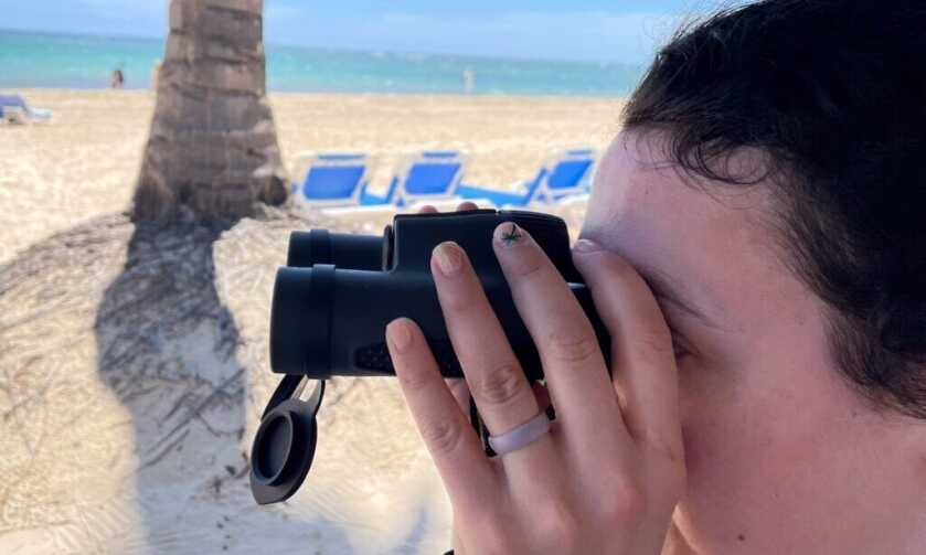 Woman using compact Vortex Triumph 10x28 HD binoculars to scan the ocean from a beach in the Dominican Republic