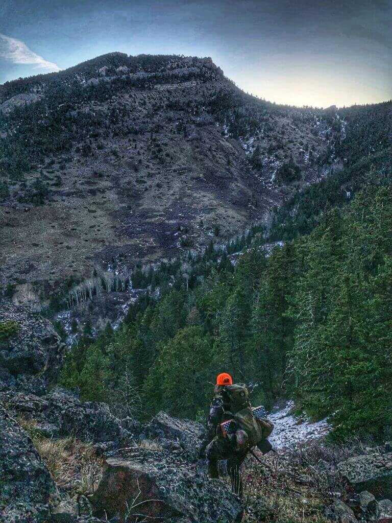 Mountain hunter carrying cold weather hunting gear through steep terrain
