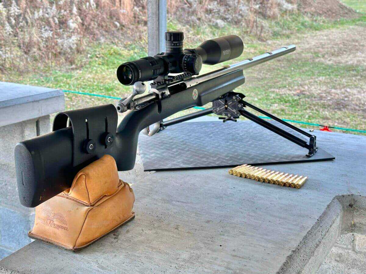 Sightron SVIII A rifle sits on a bench at the gun range, ammo layed out beside it.