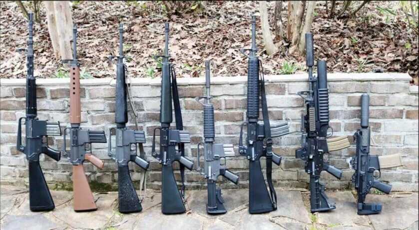 Row of AR-15 guns pointing skyward leaned against stone wall
