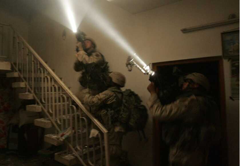 David Bellavia and two other soldiers with guns and lights going up a staircase